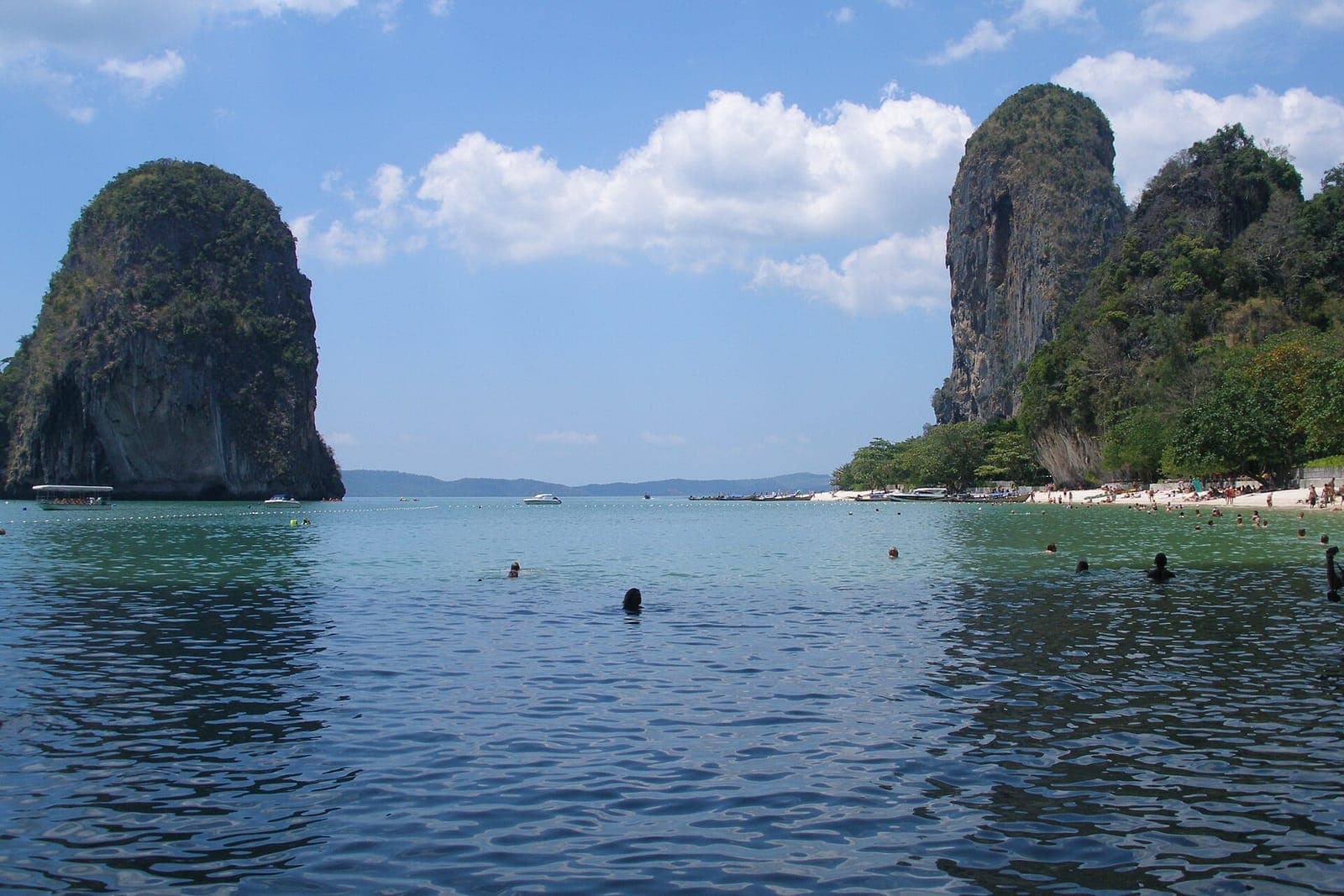 Limestone karst cliffs rising from the sea at Railay in Krabi, with swimmers in the calm water